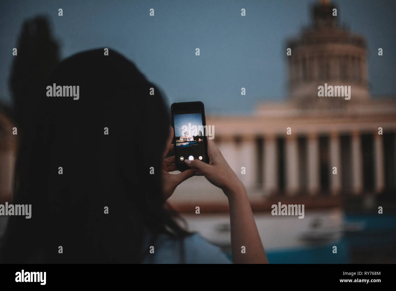 Vista posteriore della donna fotografare edificio con telefono cellulare contro il cielo durante il tramonto Foto Stock