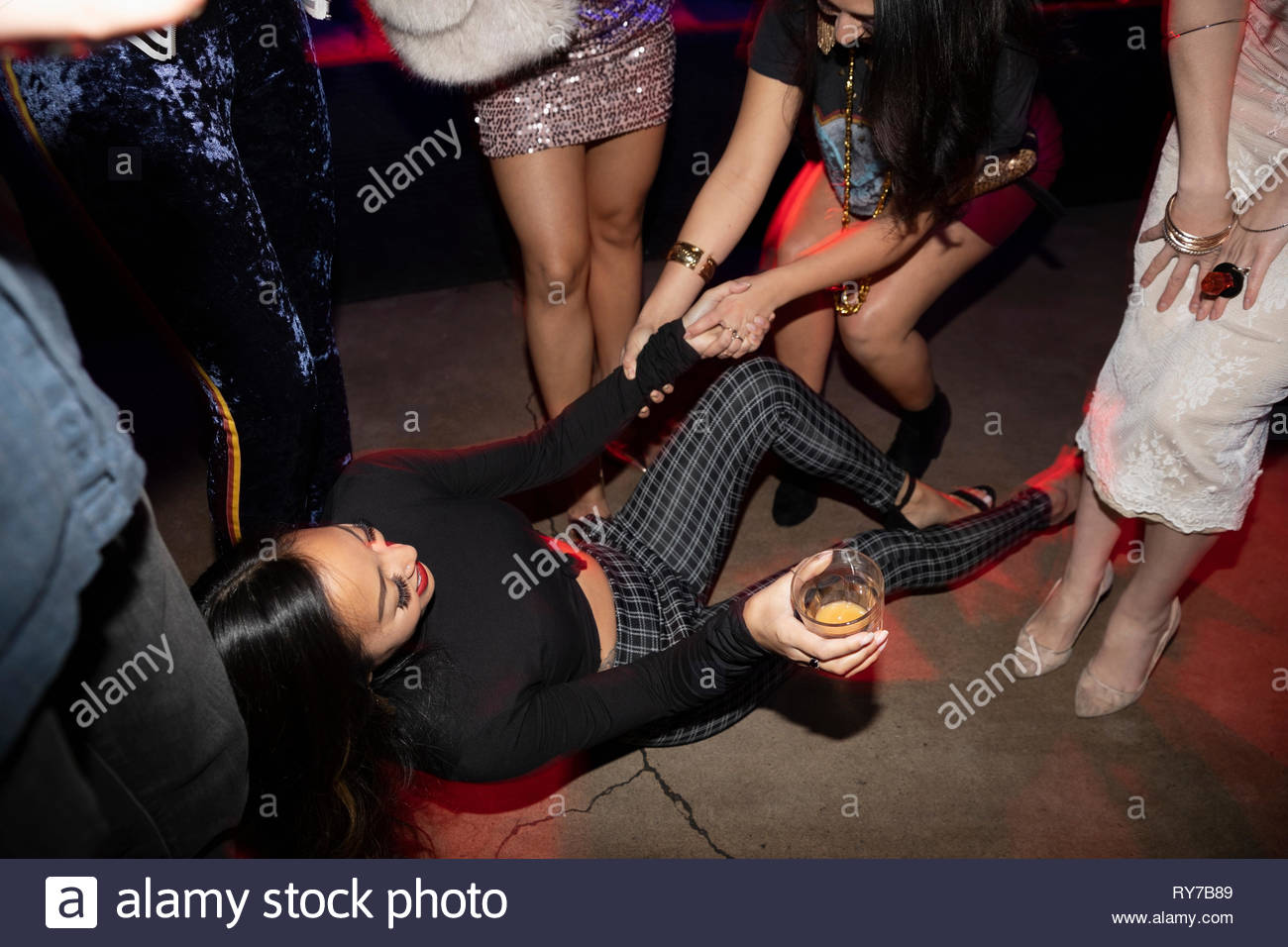 Gli amici ad aiutare la donna in caduta sul pavimento nightclub Foto Stock