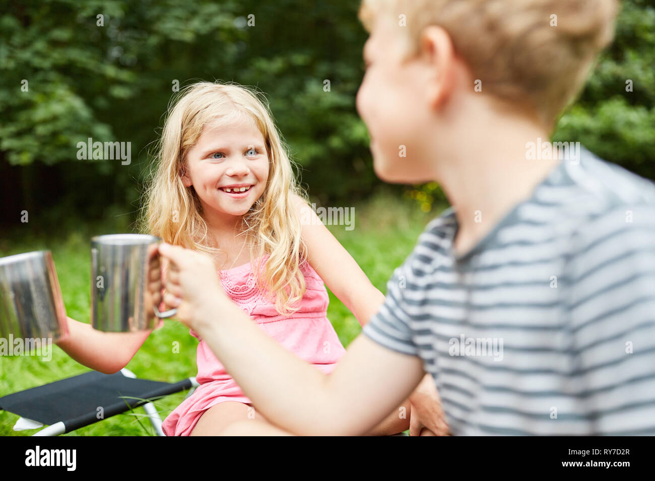 Ragazza e suo fratello presso il campeggio bere insieme da tazze Foto Stock