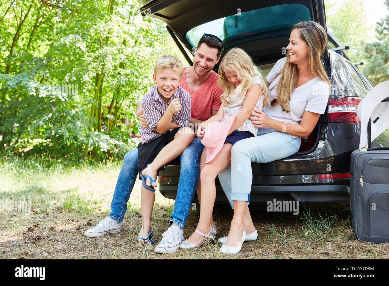 I genitori e i bambini a ridere insieme in auto prima di viaggiare durante le vacanze estive Foto Stock