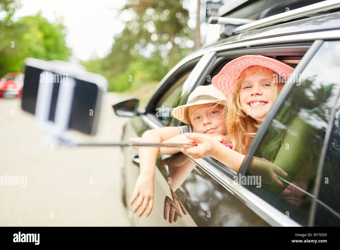 I bambini con selfie stick in auto prendendo una foto sul giro in macchina in vacanza Foto Stock