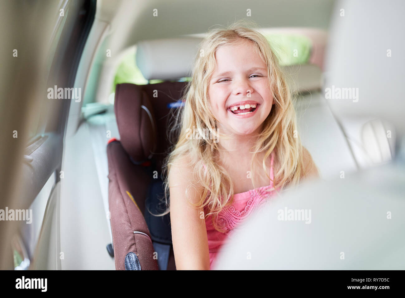 Ridere ragazza bionda nel seggiolino per bambini sul sedile posteriore in auto Foto Stock