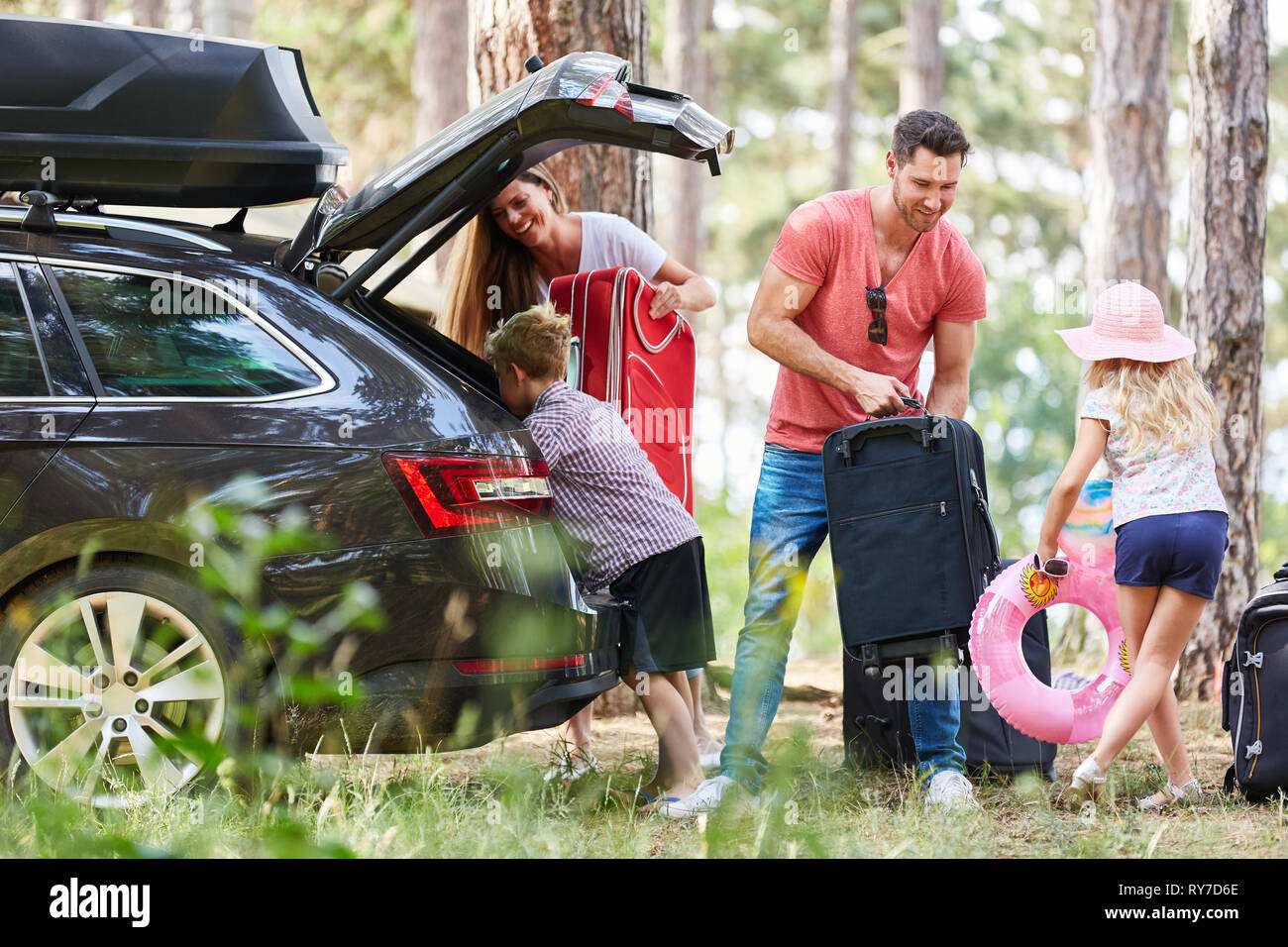 I bambini aiutano i genitori a trasportare il bagaglio per la vettura prima di viaggiare in vacanza Foto Stock