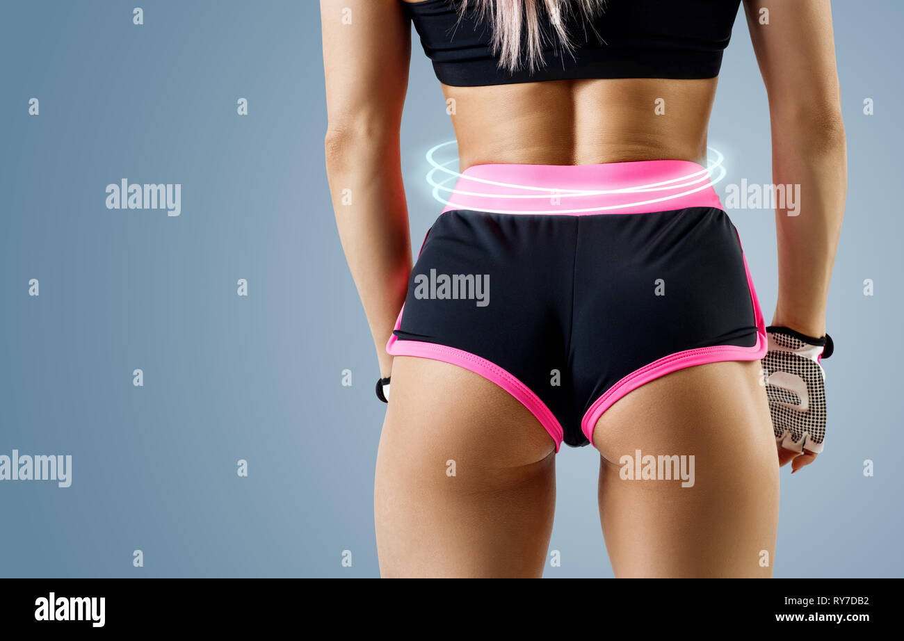 Athletic donna in abbigliamento sportivo ha dimostrato la sua perfetta muscolare di glutei. Su sfondo blu. Foto Stock