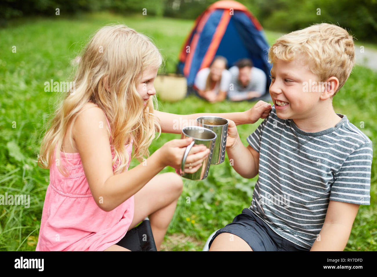 I gemelli bambini con coppe sul campeggio tease e infastidire Foto Stock