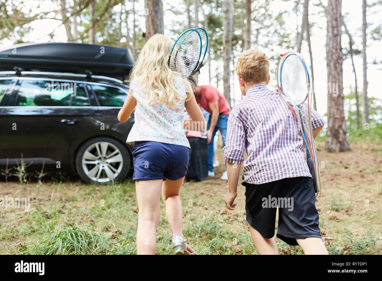 Due bambini con le racchette da badminton esegui per la vettura prima di viaggiare in vacanza Foto Stock