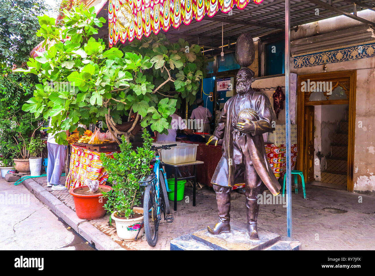 Kashgar Old Town Uyghur uomo statua tenendo un Hami melone di fronte a una strada il negozio di alimentari Foto Stock