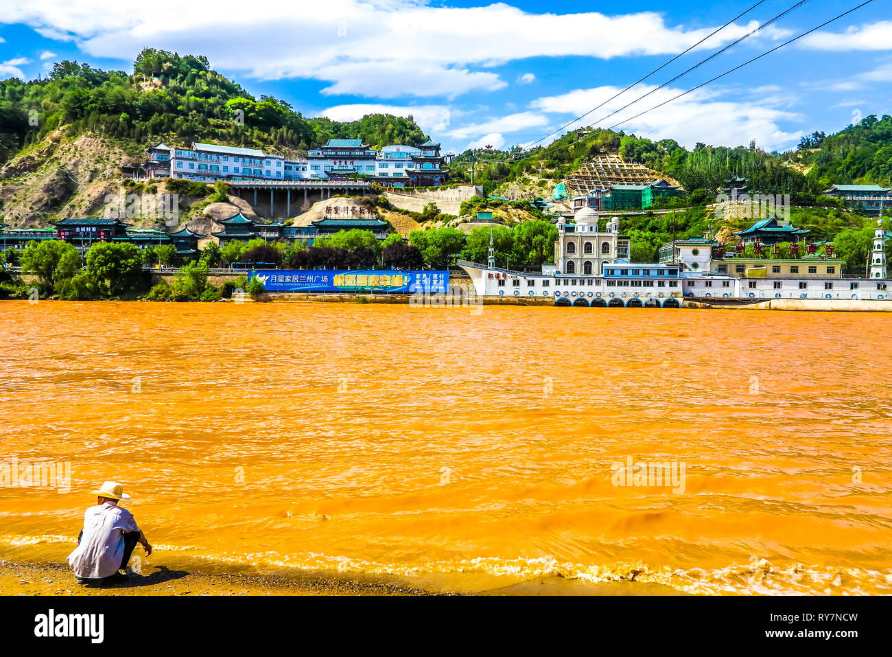 Lanzhou il Fiume Giallo Uomo cinese con Hat seduta a Riva guardando la moschea di acqua Foto Stock