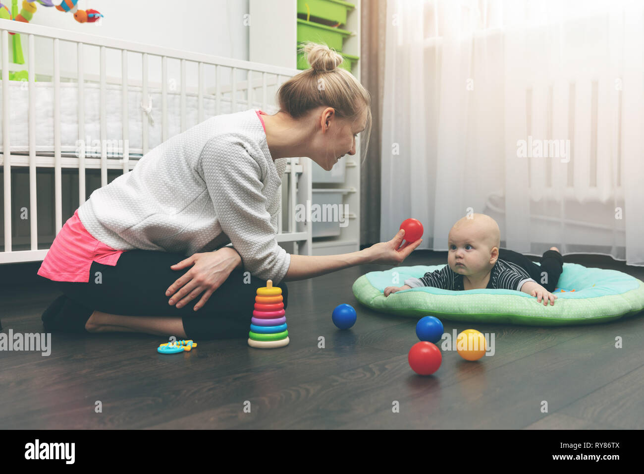 Servizio baby - nanny giocando con il piccolo bambino sul pavimento a casa Foto Stock