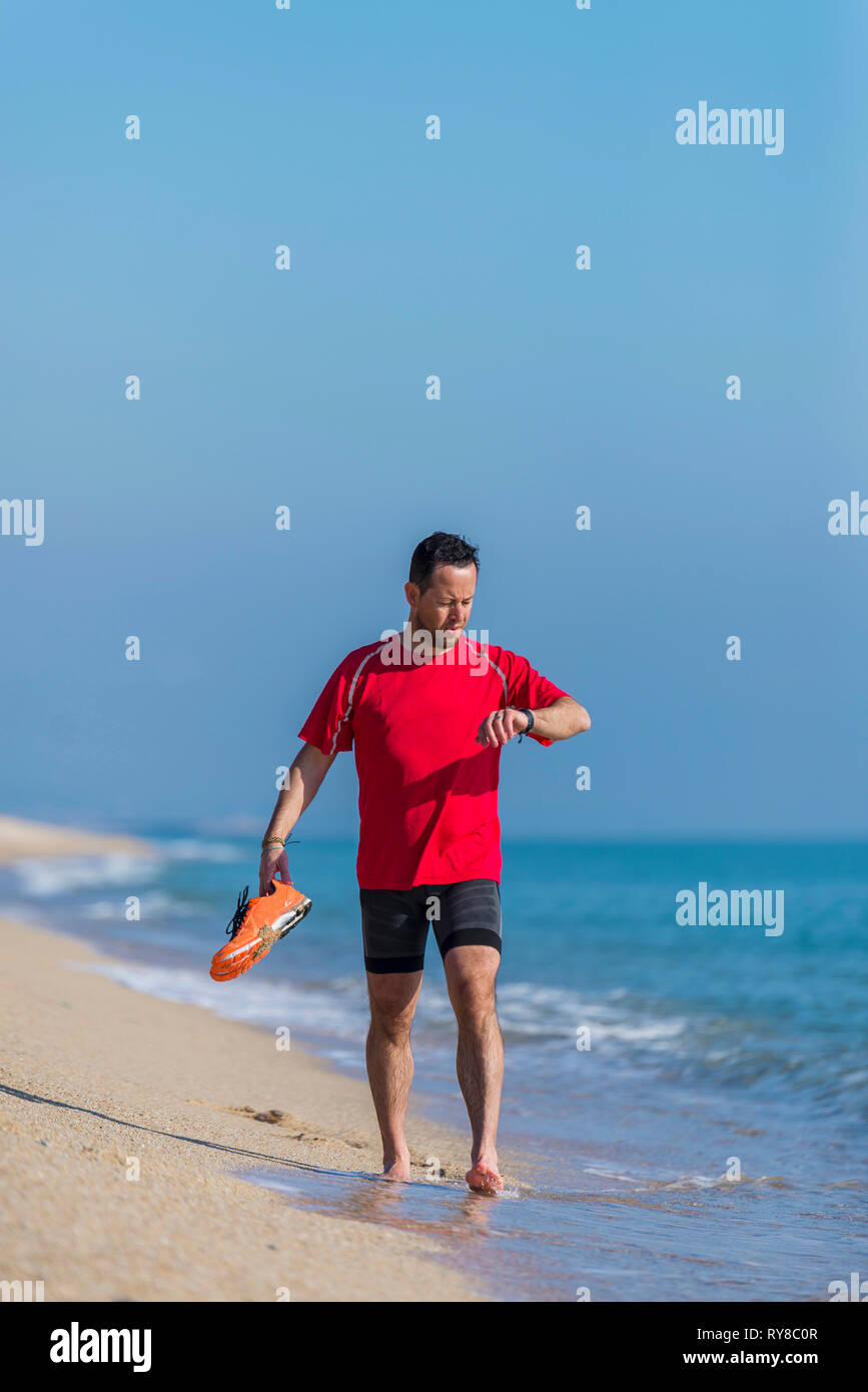 Lunghezza completa di uomo con le scarpe sportive controllo tempo mentre passeggiate in riva al mare contro sky Foto Stock