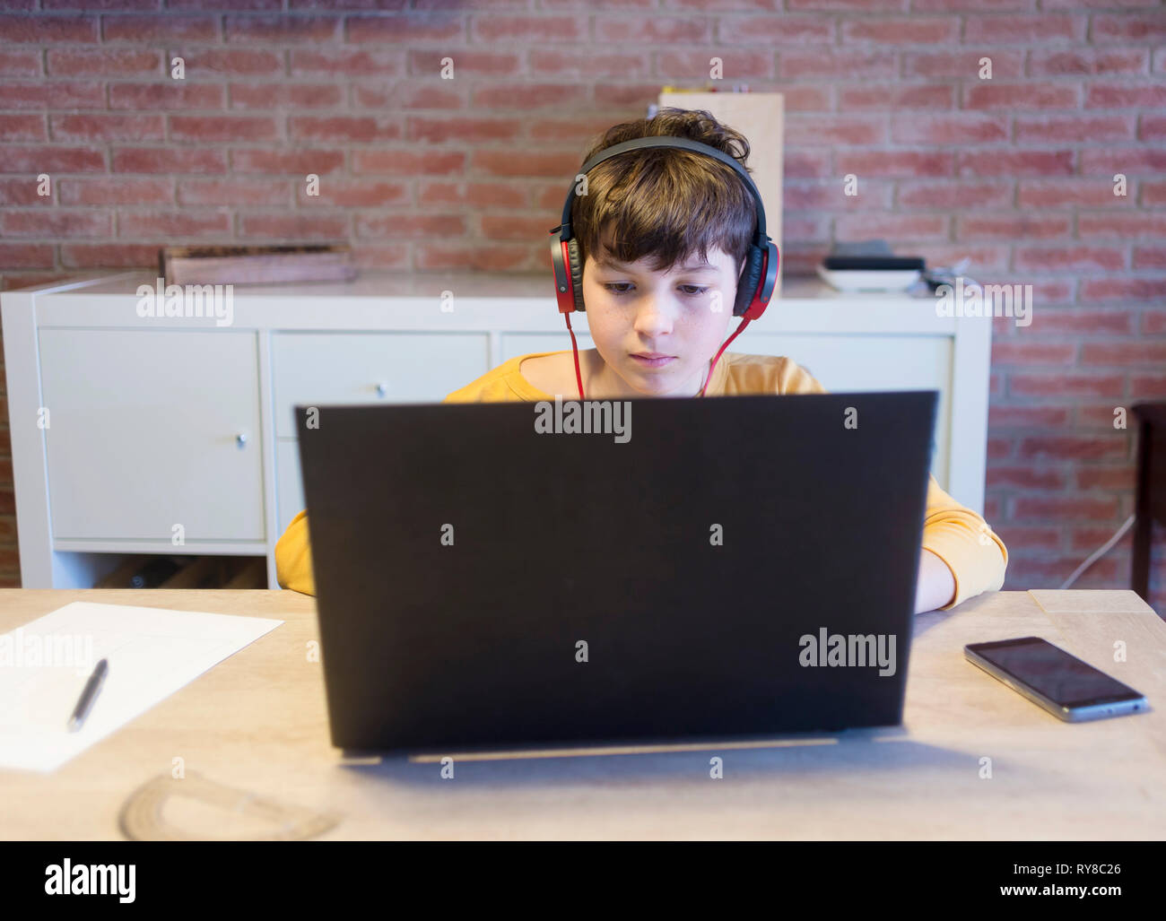 Ragazzo serio apprendimento utilizzando il computer portatile e le cuffie a casa Foto Stock