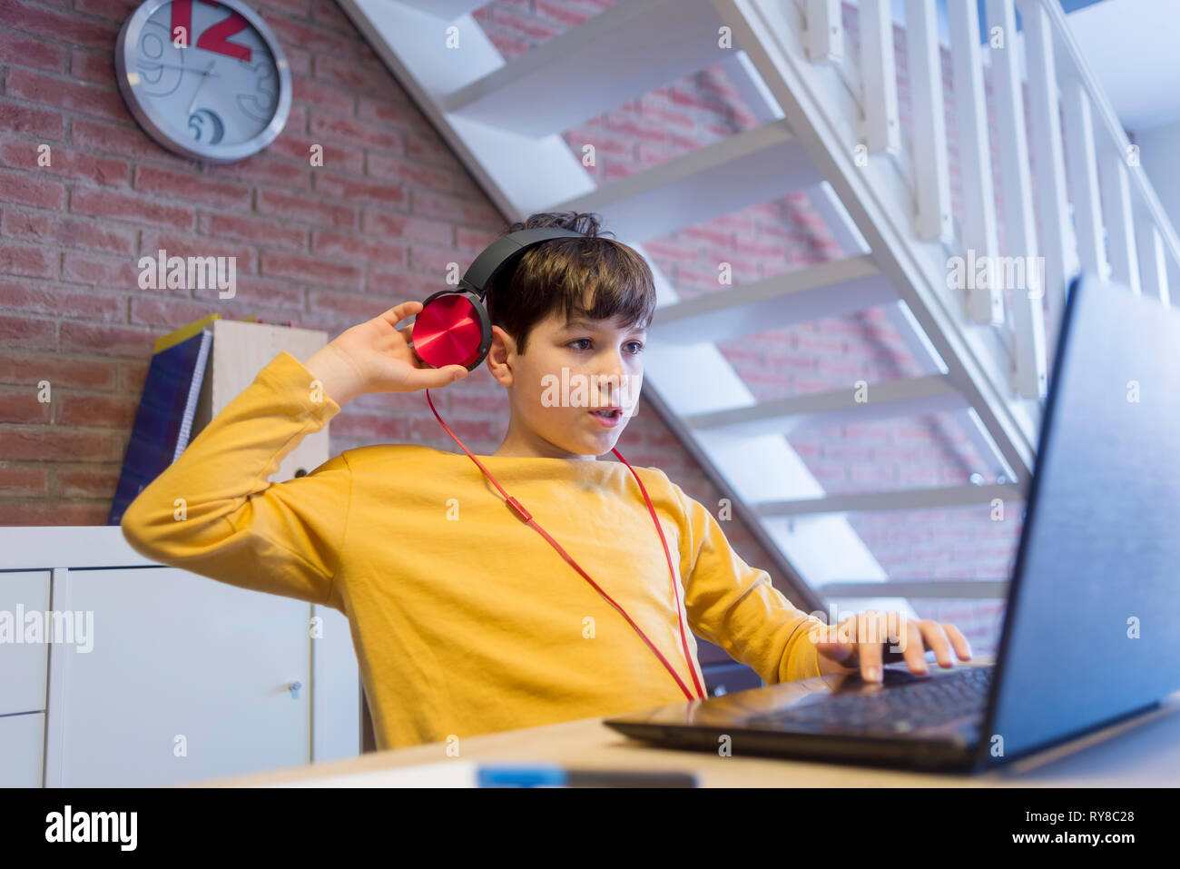 Ragazzo facendo i compiti utilizzando le cuffie e computer portatile a casa Foto Stock