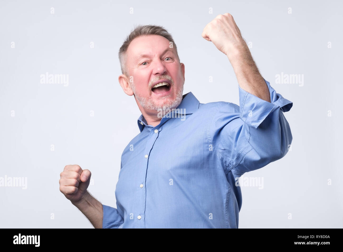 Felice senior uomo forte sollevamento rinserrata pugni in urrà gesto, trionfante Foto Stock