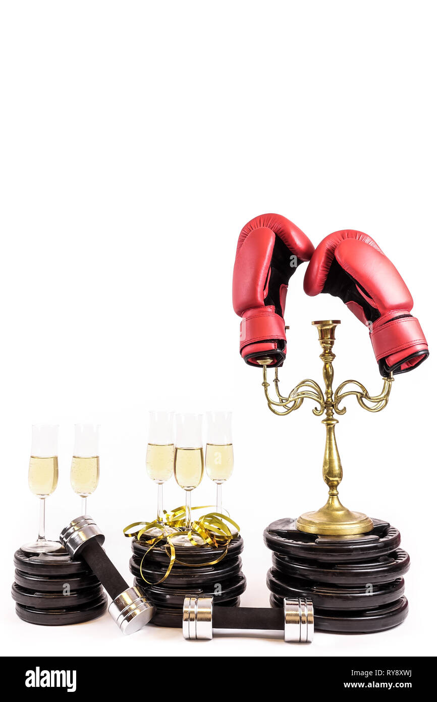 Nuovo anno risoluzione. Festeggiare il capodanno in palestra. Bicchieri di champagne su piastre di peso e manubri. I guantoni candelabri. Allenamento e Foto Stock
