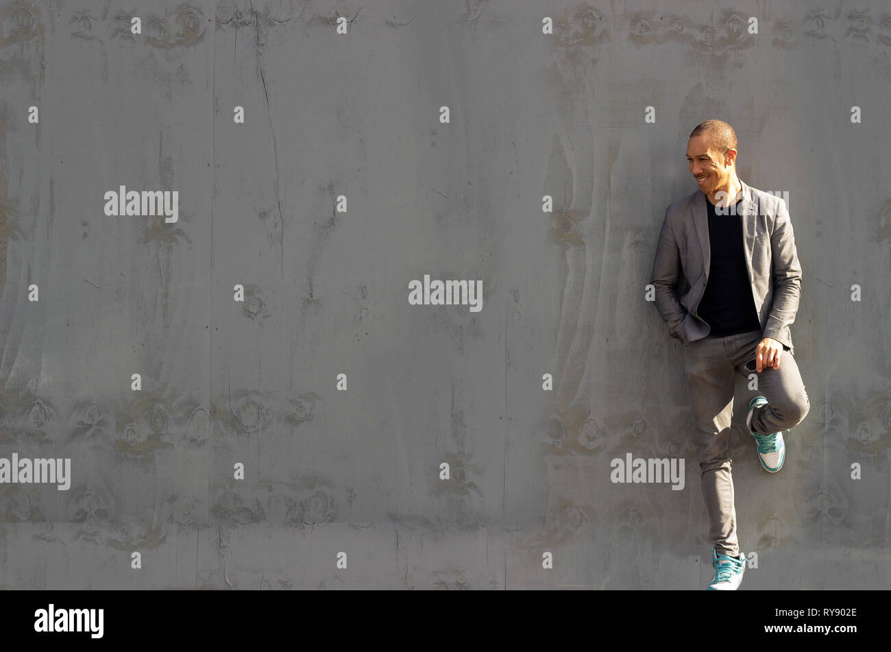 Cool guy appoggiata contro un verniciato di colore grigio a parete in legno, spruzzata in presenza di luce solare Foto Stock