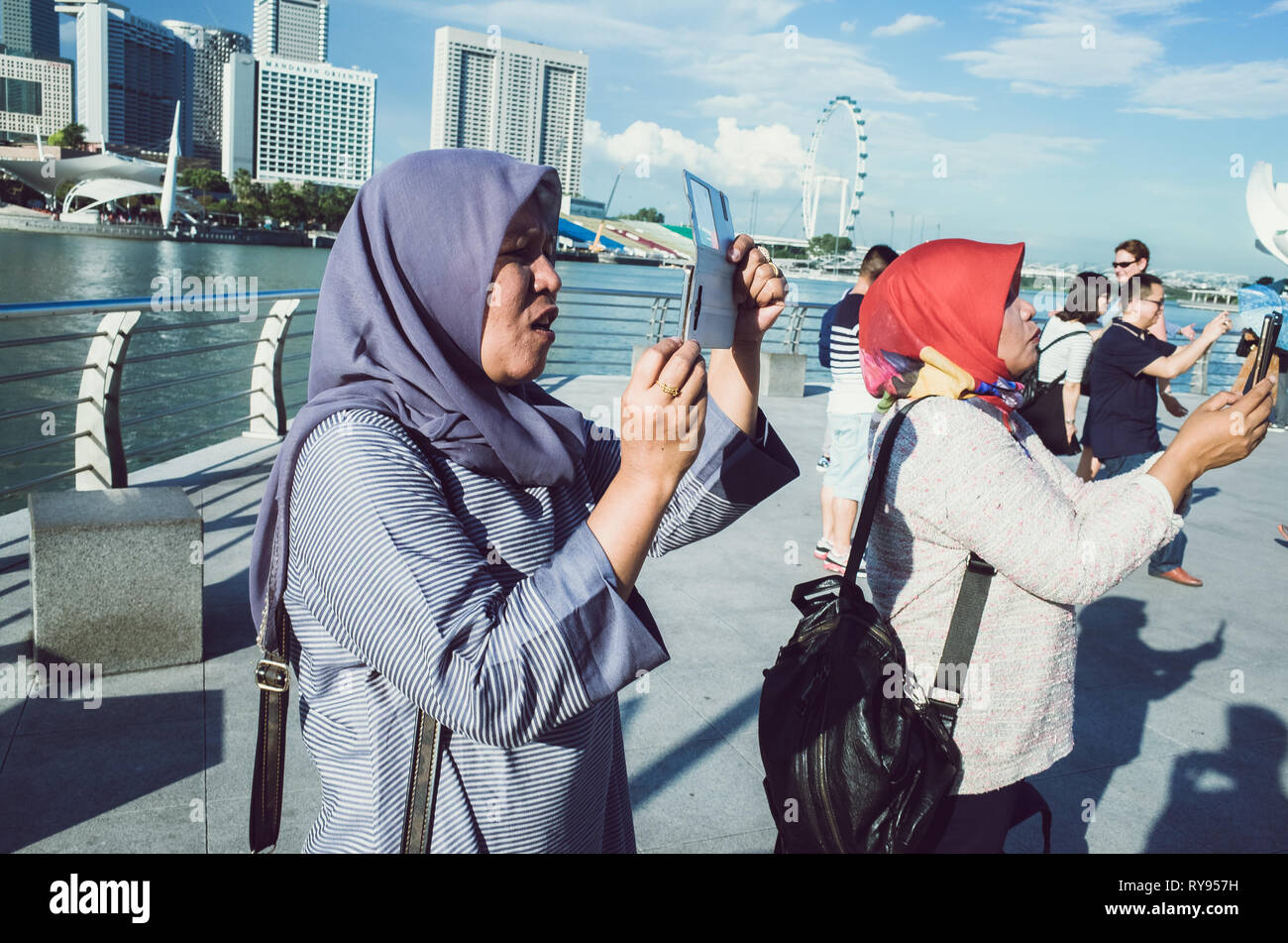 Turismo musulmano le donne in viola e rosso hijabs, tenendo le foto delle vacanze di Marina Bay, Singapore Foto Stock