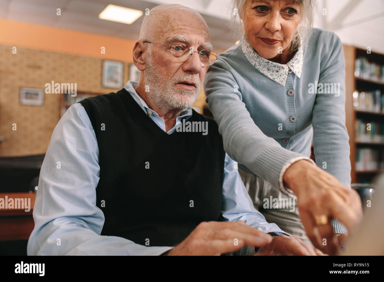 Senior donna rivolta verso lo schermo di un computer mentre un uomo anziano guarda. Coppia senior presso una libreria utilizzando un computer. Foto Stock
