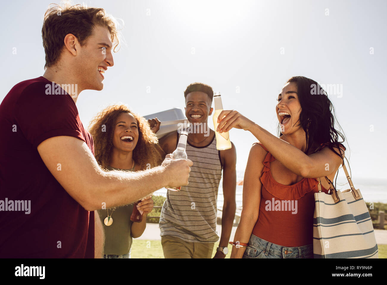 Gruppo di multi-etnico amici avente birre mentre passeggiate per il picnic. Gli uomini e le donne amici andare su un picnic su un giorno d'estate. Foto Stock