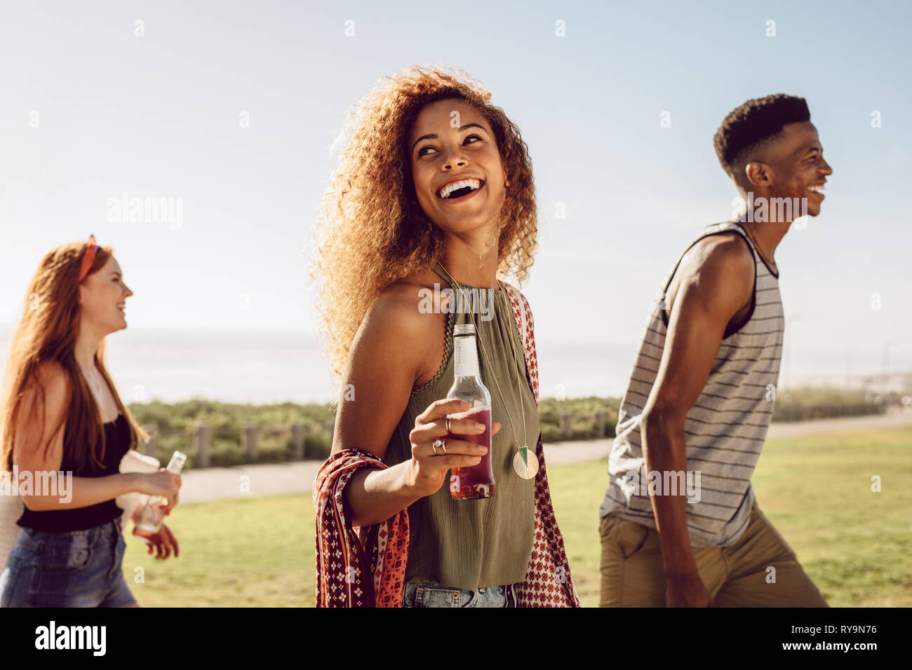 Bella giovane donna con birra a piedi con gli amici all'aperto su un giorno d'estate. Femmina di appendere fuori con gli amici all'esterno. Foto Stock