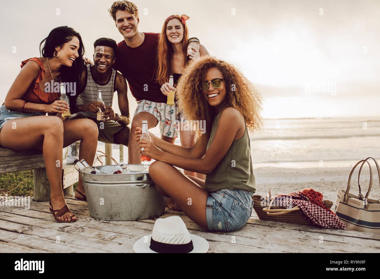 I giovani intorno a vasca di bevanda seduto alla spiaggia. Belle Donne con amici appendere fuori a beach in vacanza. Foto Stock
