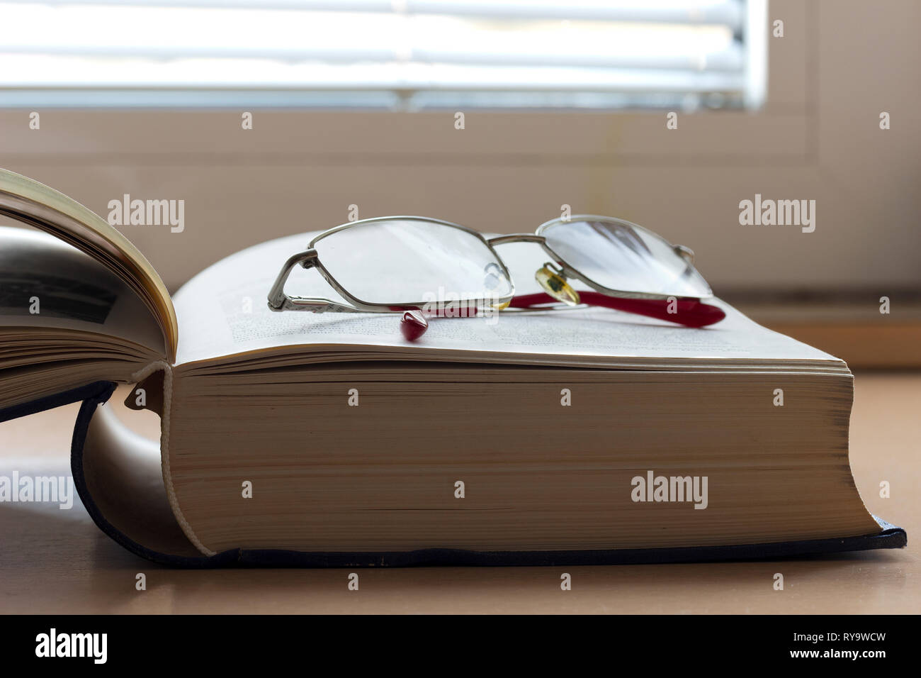 Libro aperto su un tavolo con gli occhiali da lettura Foto Stock