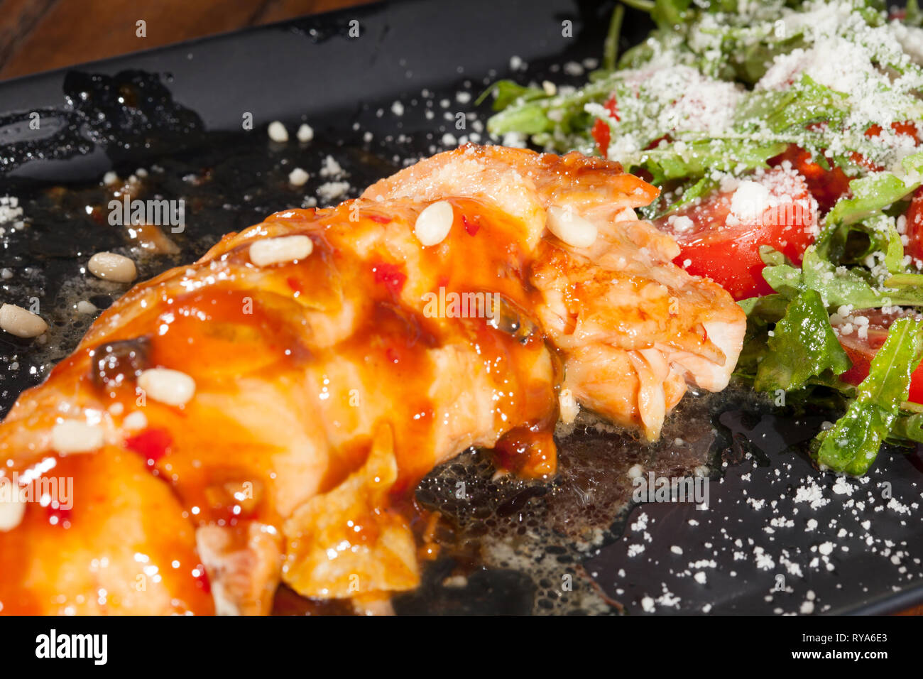 Calamari cotti a base di pesce serviti con pomodori prezzemolo tagliati formaggio e salsa al nero sulla piastra di argilla sul tavolo di legno Foto Stock