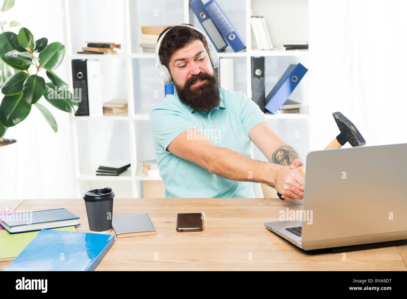 Computer lag. Ragioni per computer in ritardo. Come fissare il lento sistema di ritardo. Odio di ufficio di routine. Uomo Barbuto guy ufficio cuffie swing martello sul comput Foto Stock