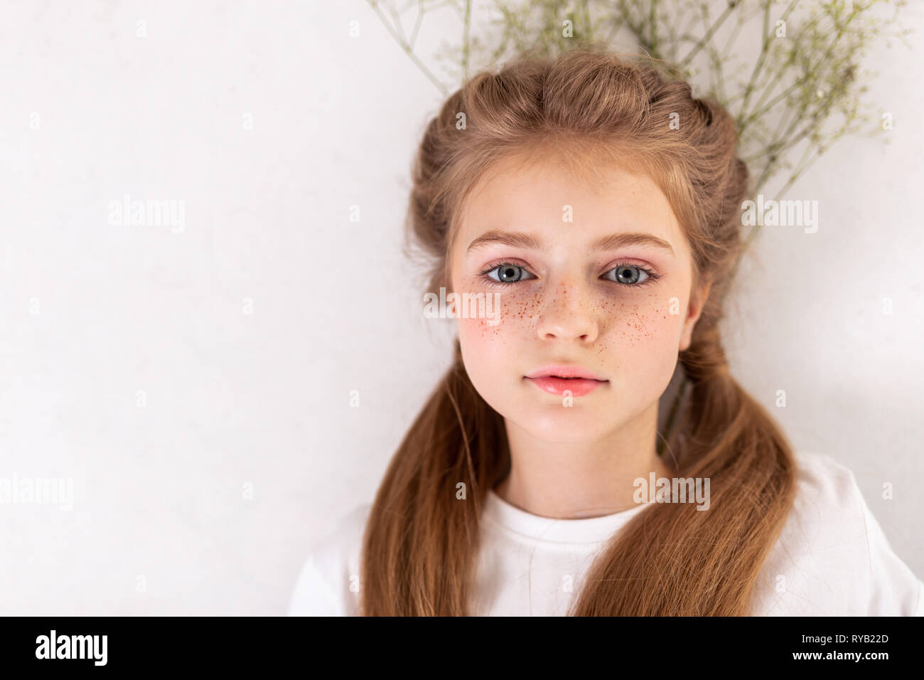 Graziosa bambina con viso carino giacente sul piano con fiori Foto Stock