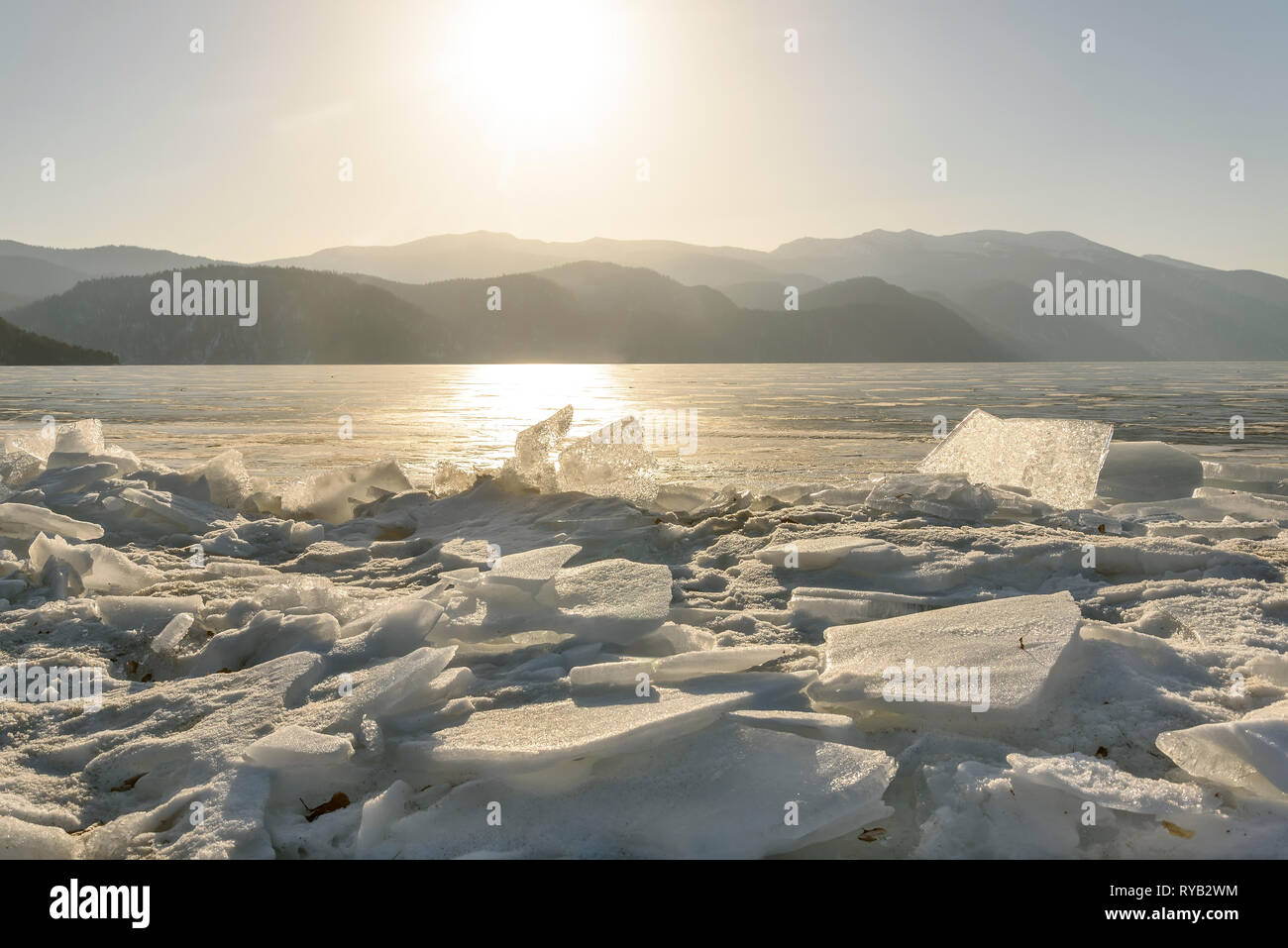 Bellissima vista del lago ghiacciato Teletskoye con ghiaccio, floes e il sole sopra le montagne su una mattina di sole Foto Stock