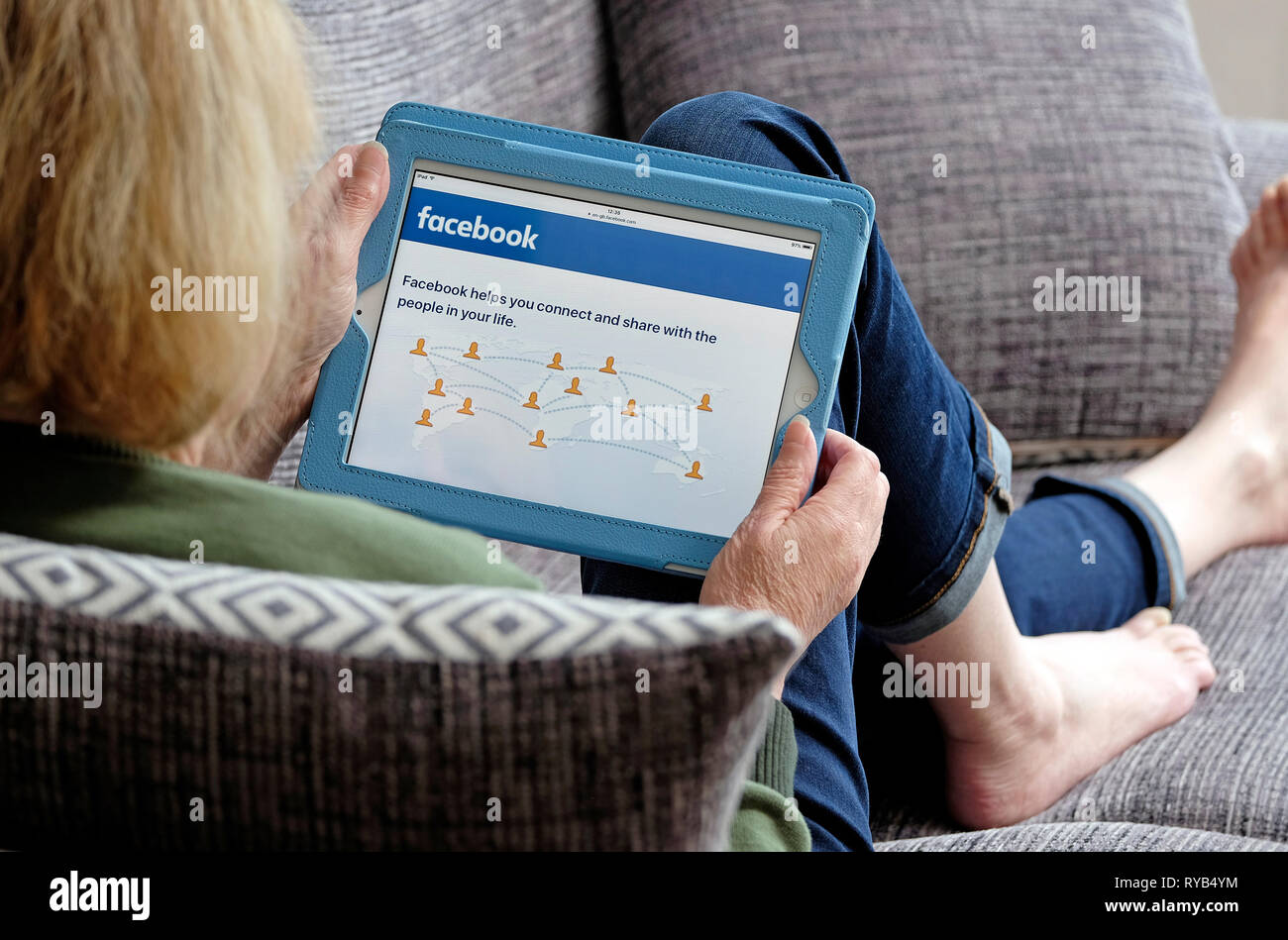 Persona in possesso di computer tablet recante sul divano guardando il sito web Foto Stock