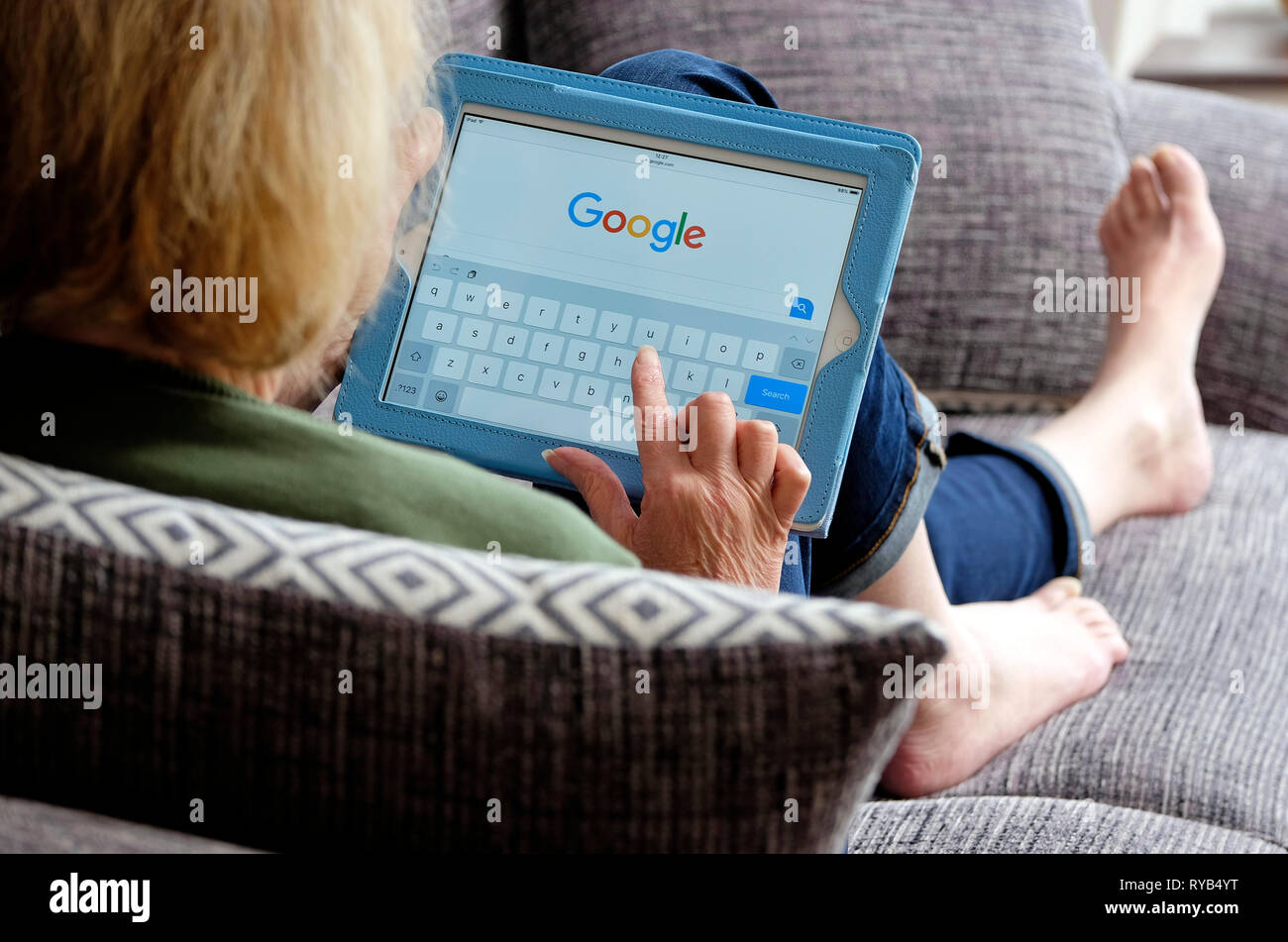 Persona in possesso di computer tablet recante sul divano guardando il sito web Foto Stock