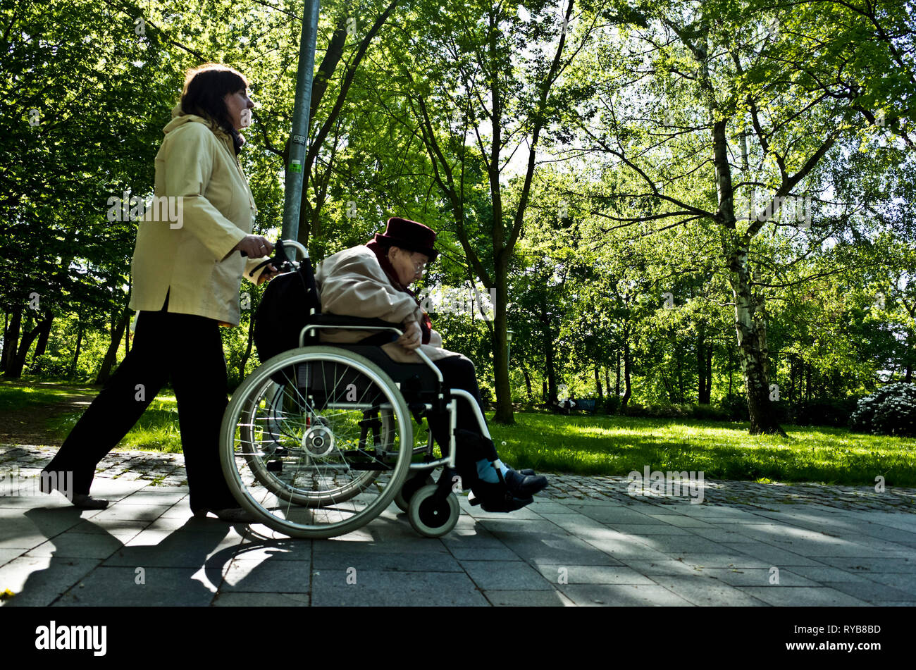 Helper spingendo un anziano donna disabile su sedia a rotelle nel parco Foto Stock