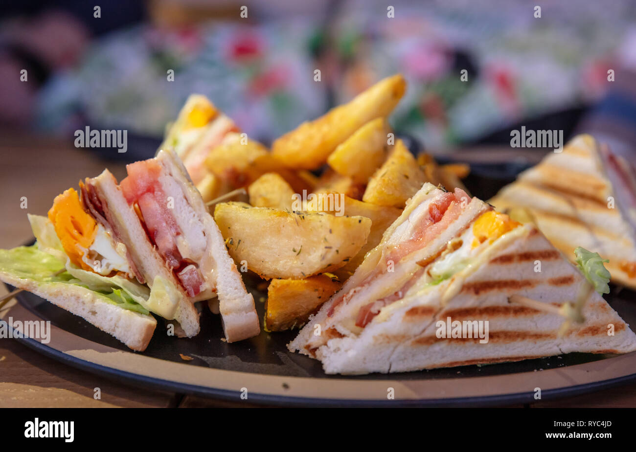 Club sandwich, prendere via il cibo. Fette di pane, formaggio, prosciutto, uova, lattuga, patatine fritte, primo piano Foto Stock