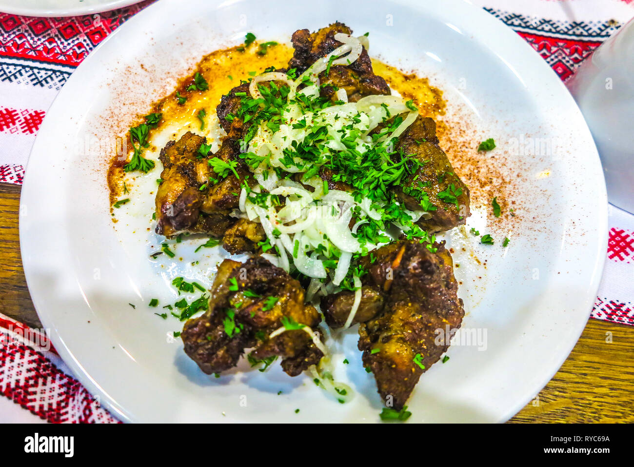 Ukrainian tradizionale stile dei Carpazi agnello arrosto guarnito con cipolle e prezzemolo su una piastra bianca Foto Stock