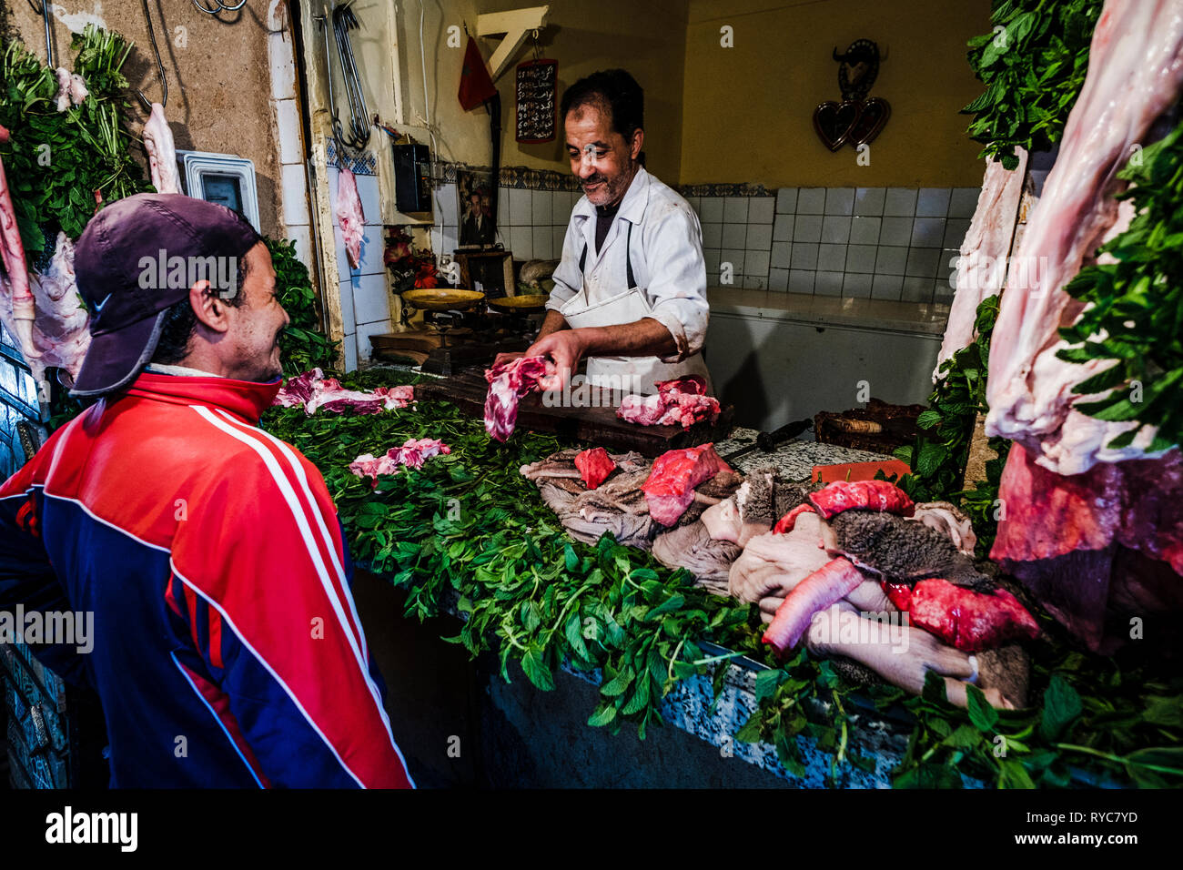 Un macellaio che serve un cliente dal suo stallo nella medina di Marrakech, Nord Africa Foto Stock