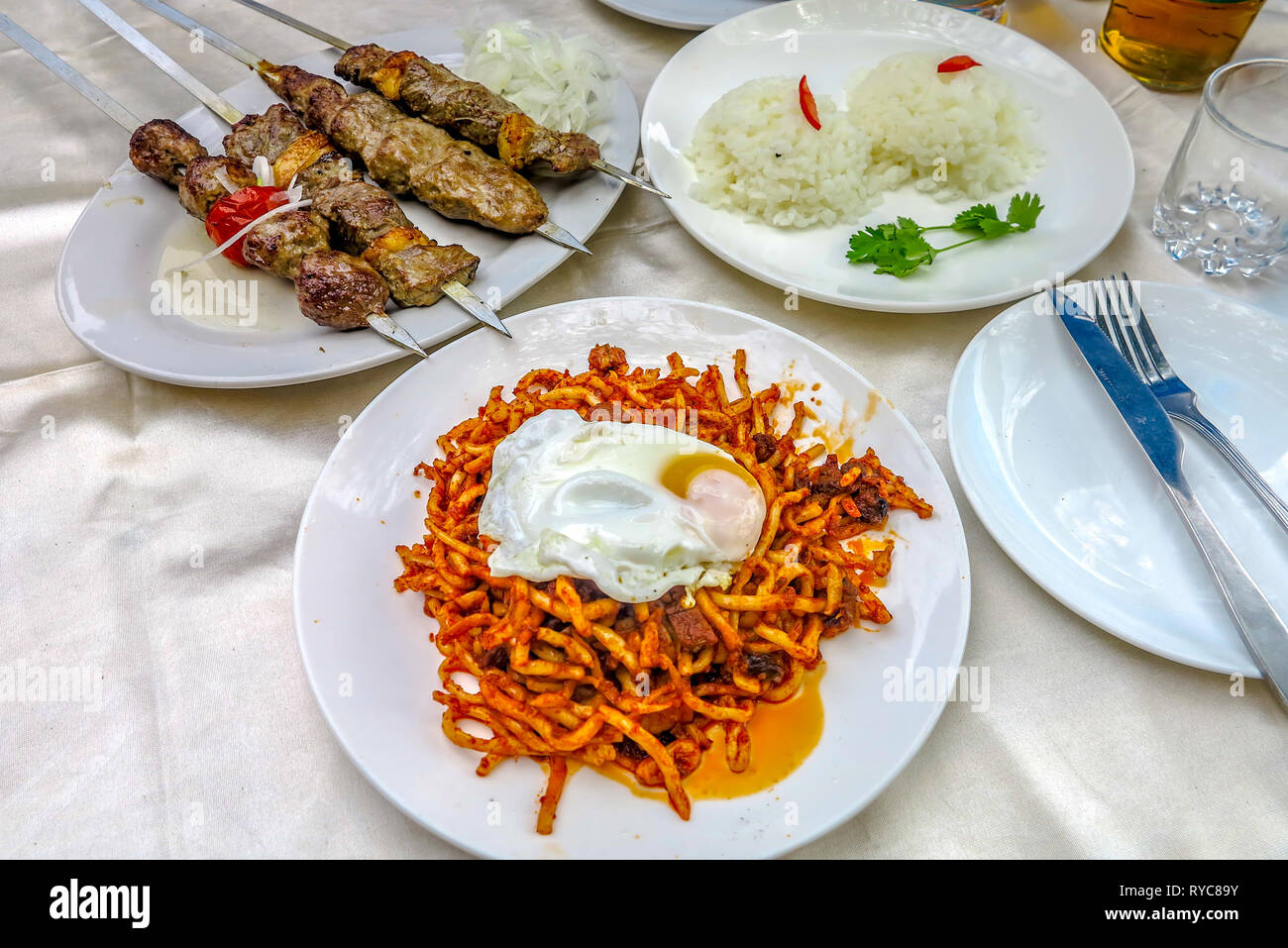 Uzbek tradizionali spiedini di agnello con riso e fritti Lagman piccante tagliatelle piatto con le uova in camicia Foto Stock