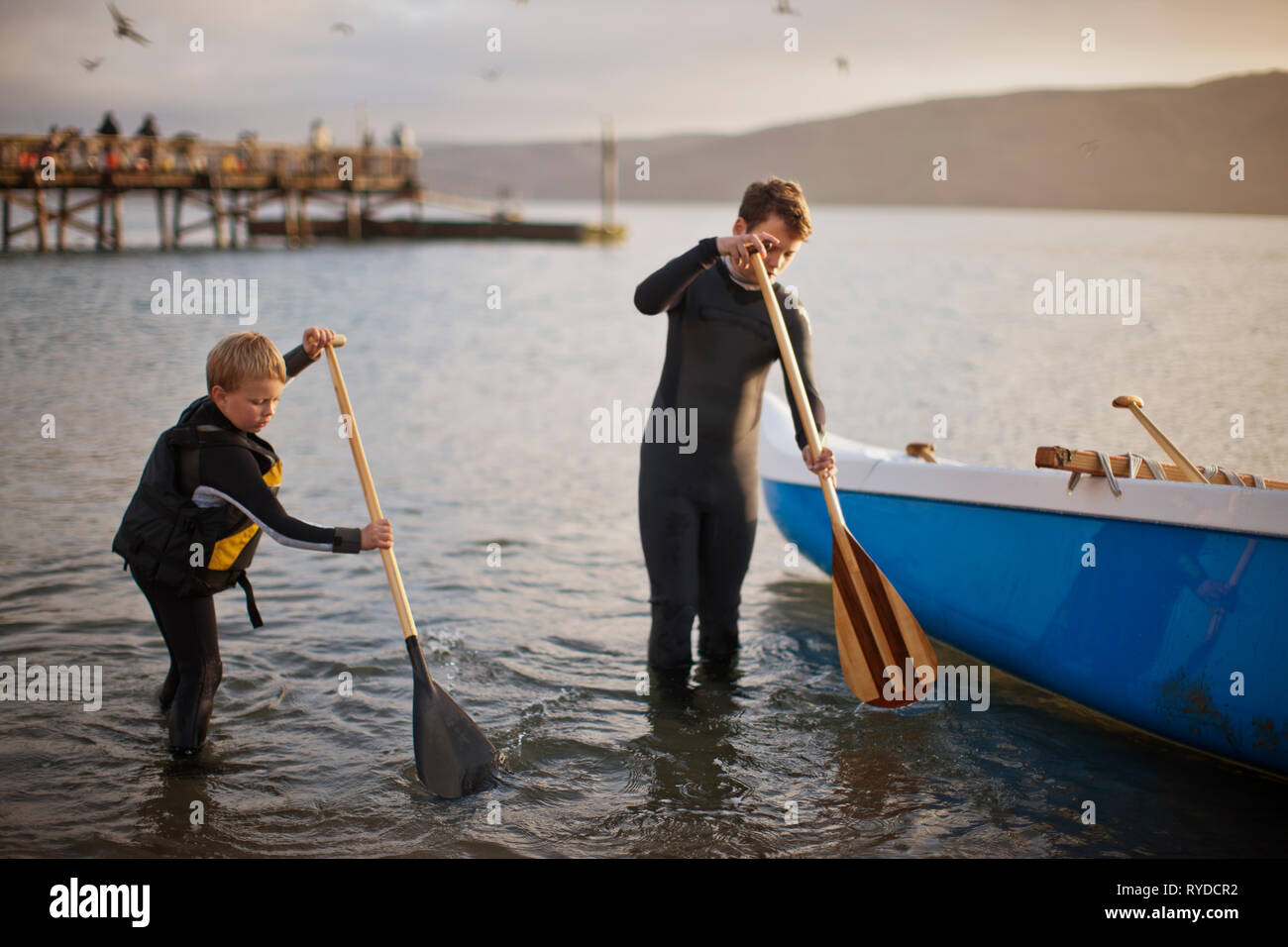 Due fratelli giocando con i remi in acqua poco profonda. Foto Stock