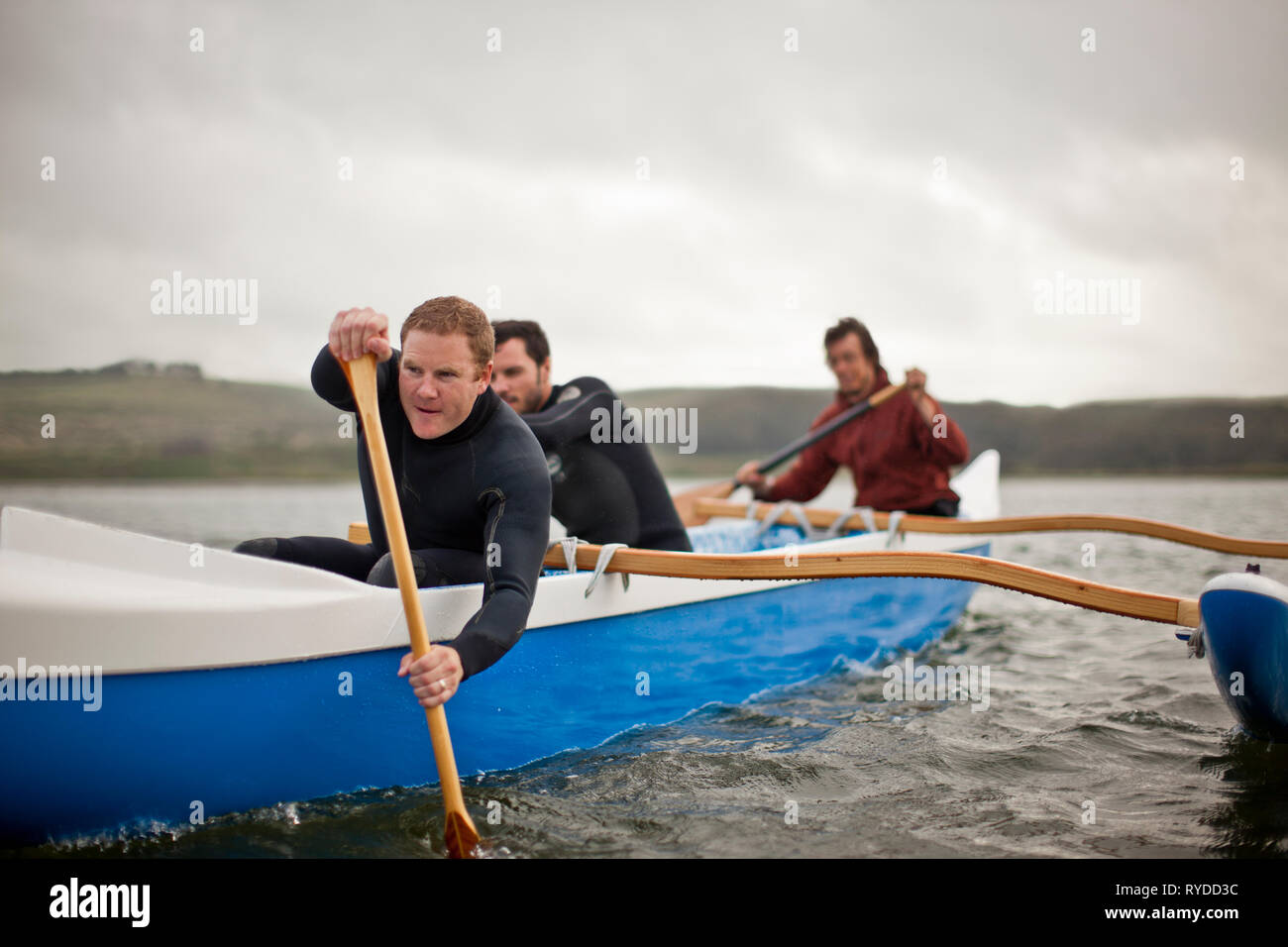 Tre giovani adulti pagaiando insieme in una canoa sulle sponde di un lago. Foto Stock