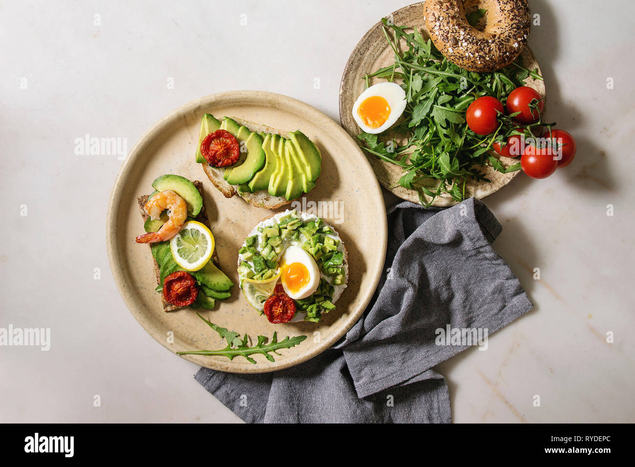 Varietà di panini vegetariani con fette di avocado, pomodori secchi, uovo, gamberetti, rucola servita su piastra in ceramica oltre bianco grigio maculato backgr Foto Stock