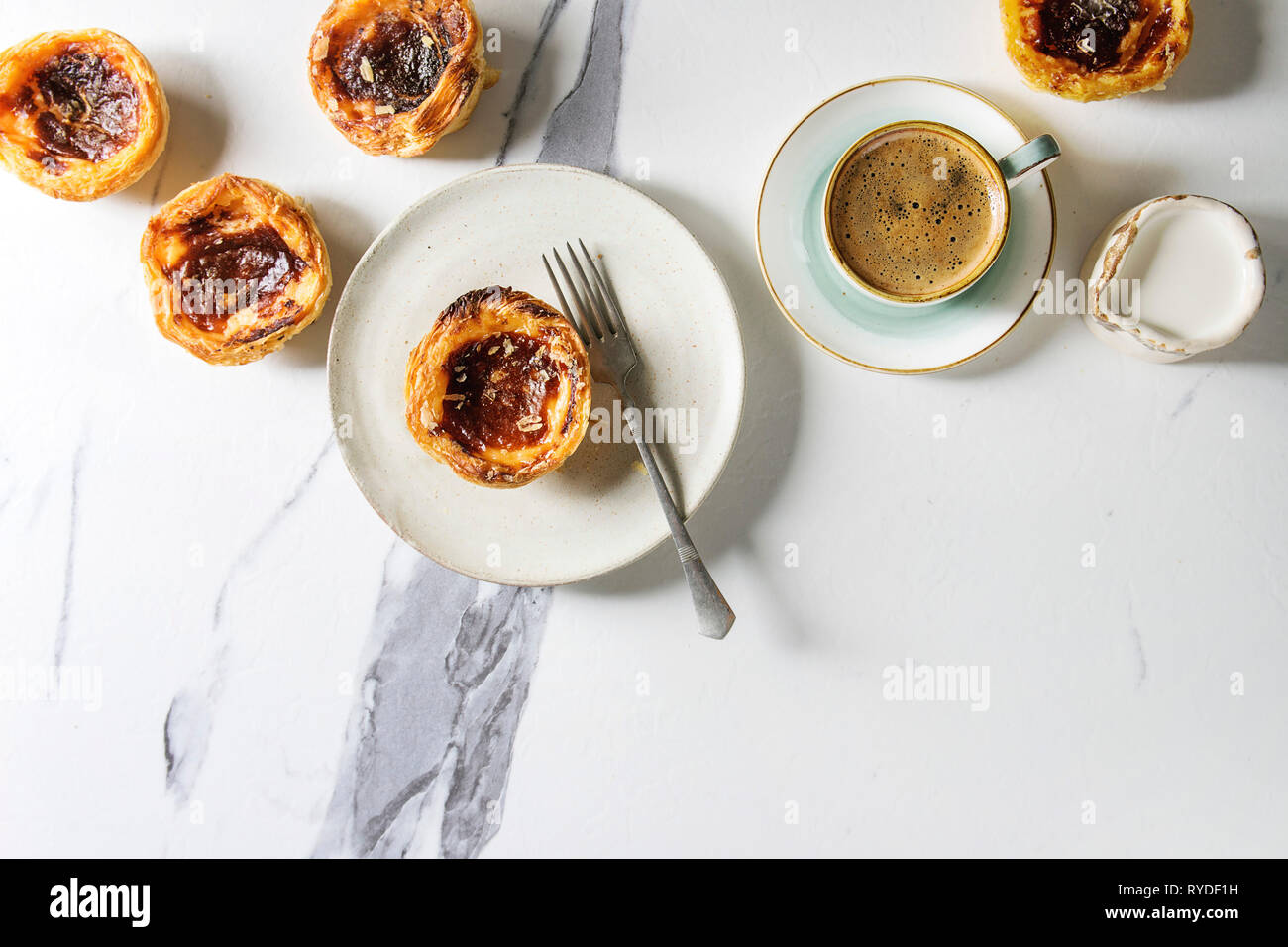 Tradizionale portoghese crostata di uova dessert pastello Pasteis de nata con la tazza di caffè nero e la brocca del latte su marmo bianco dello sfondo. Laici piana, spazio Foto Stock