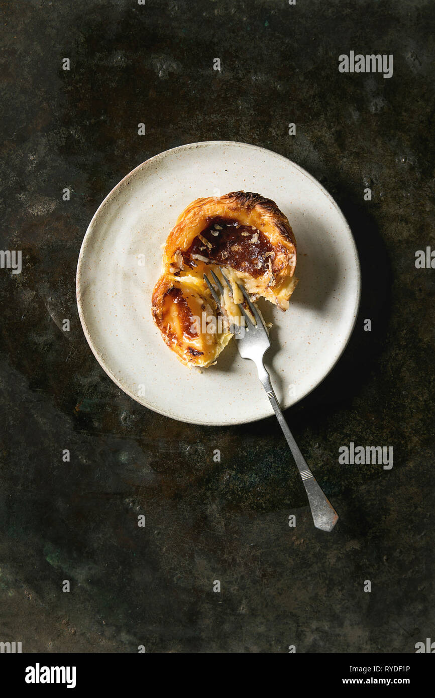 Rotte portoghesi tradizionali crostata di uova dessert pastello Pasteis de nata su piastra in ceramica con la forcella più metallo scuro dello sfondo. Laici piana, spazio Foto Stock
