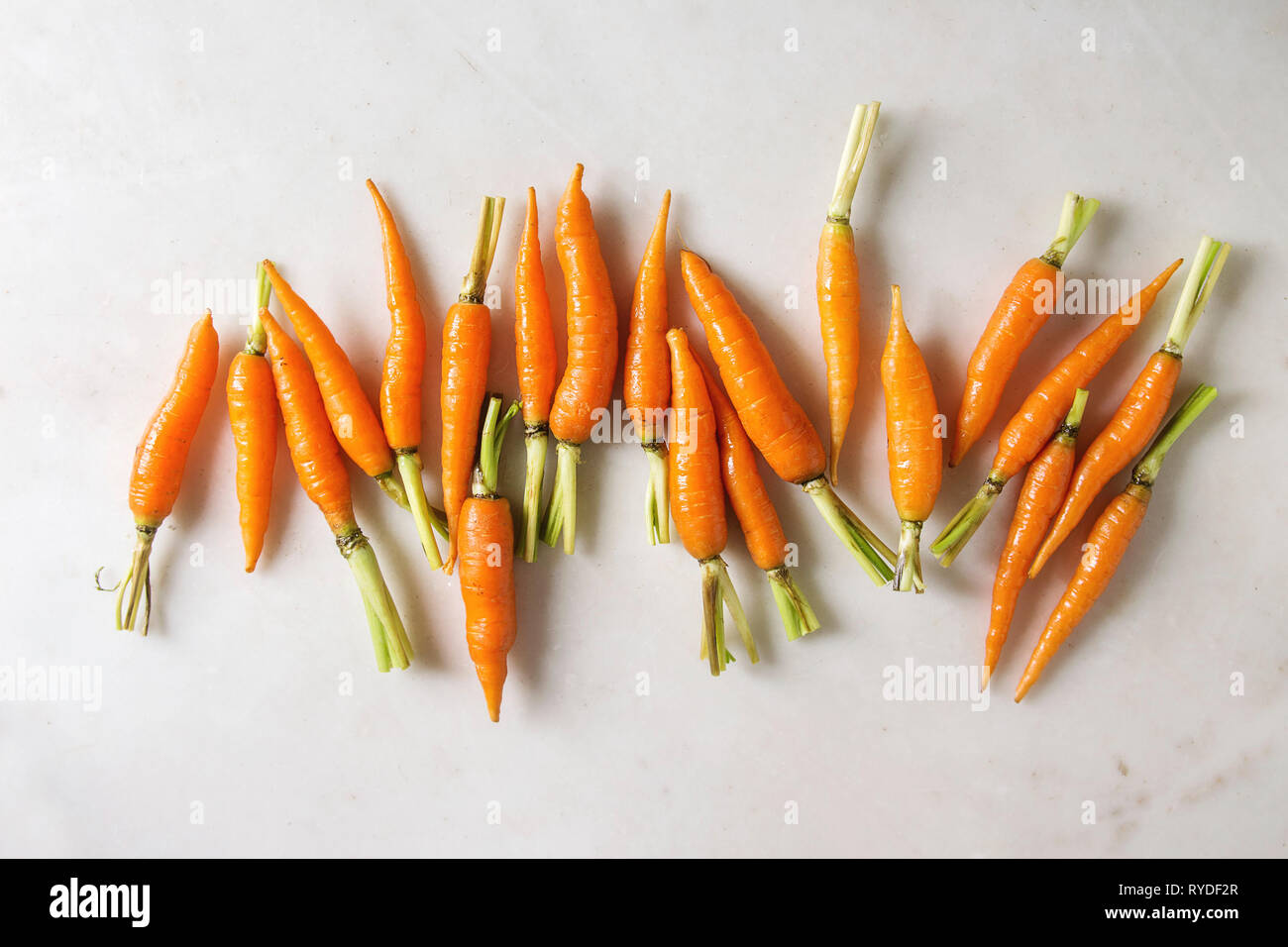 Giovani mini carota in fila su marmo bianco dello sfondo. Appartamento laico, spazio. Concetto di cucina a vista, cibo sfondo. Foto Stock