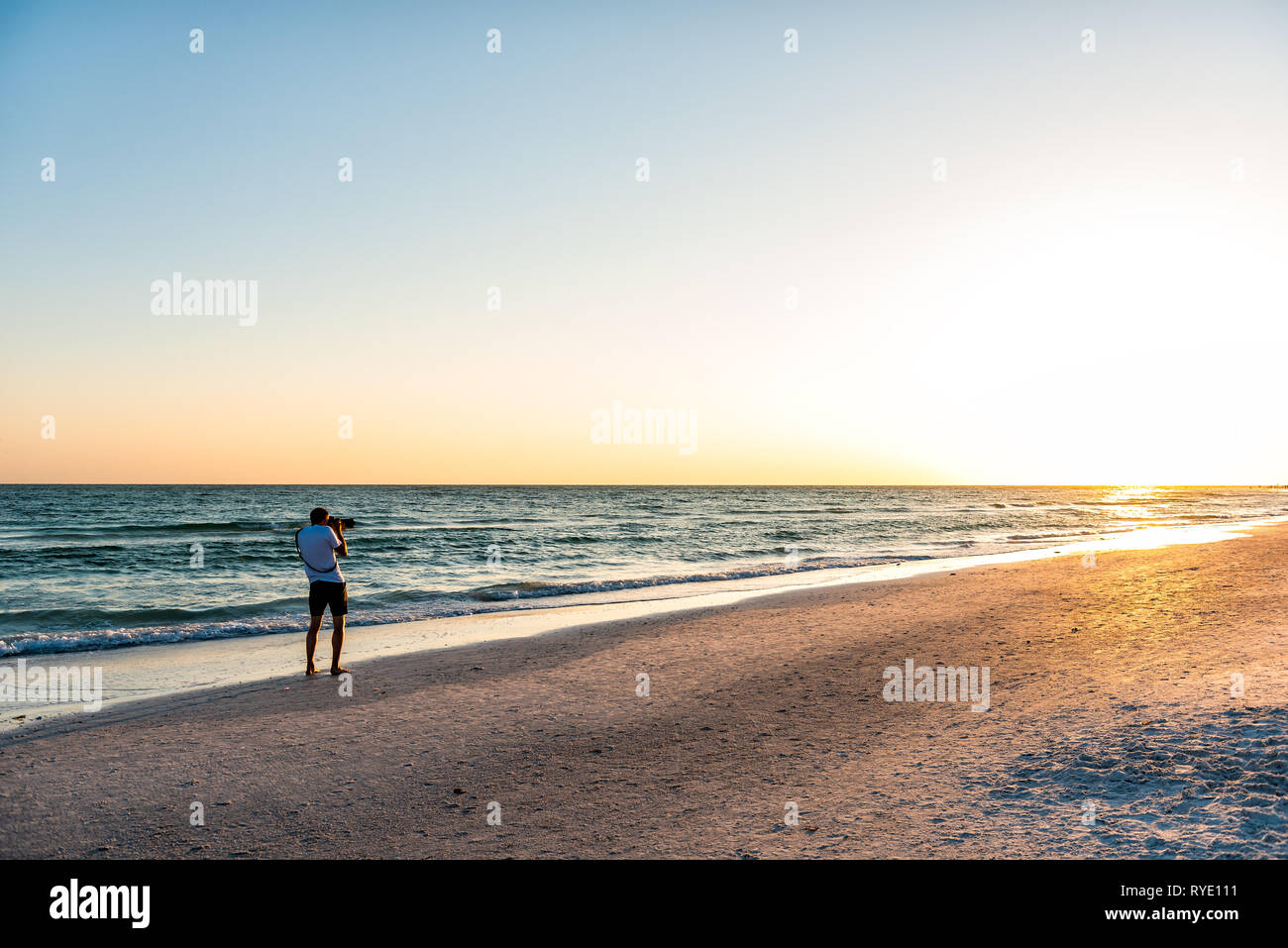 Giovane fotografo professionista sta immagine foto del tramonto sulla spiaggia in Florida Siesta Key da Sarasota da spiaggia onde tengono grande fotocamera Foto Stock