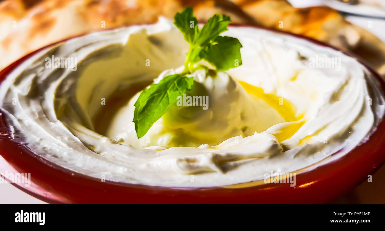 Labneh, una spessa e cremosa salsa di yogurt con foglie di menta e olio d'oliva. Cibo libanese e mediorientale. Vista ravvicinata di un sano pasto mediterraneo. Foto Stock