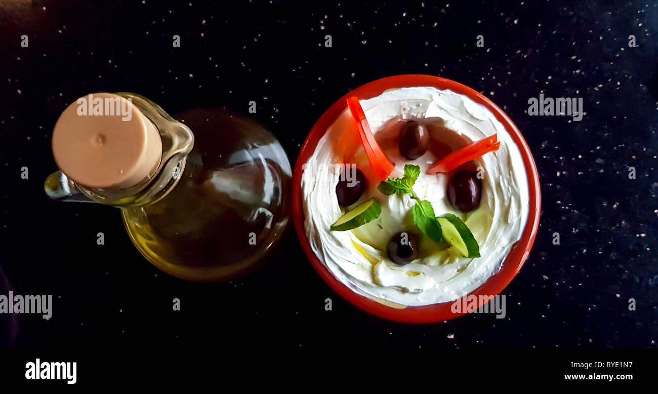 Una ciotola di labneh, un bagno arabo di formaggio crema di yogurt, con verdure e una bottiglia di olio d'oliva su un tavolo. Cucina mediorientale. Foto Stock