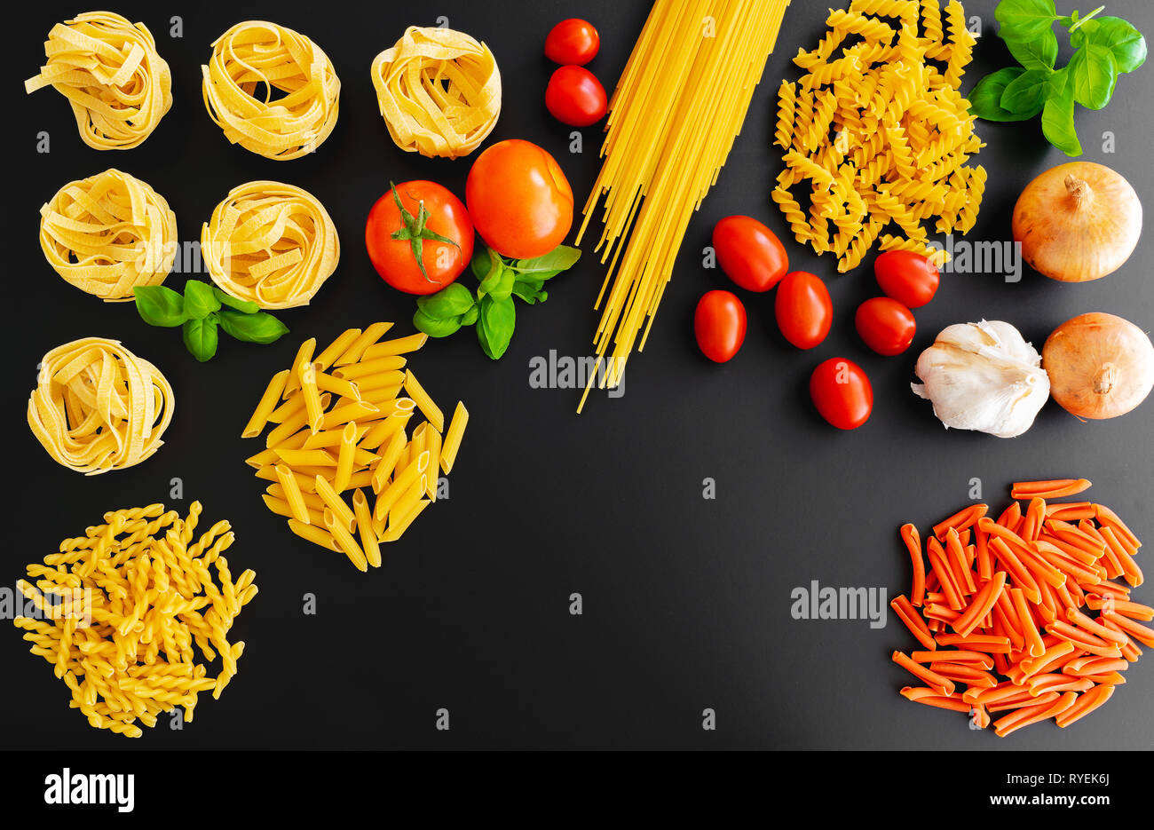 Non cotte diversi piatti di pasta italiana tagliatelle su sfondo scuro con foglie di basilico fresco, pomodori e cipolle Foto Stock