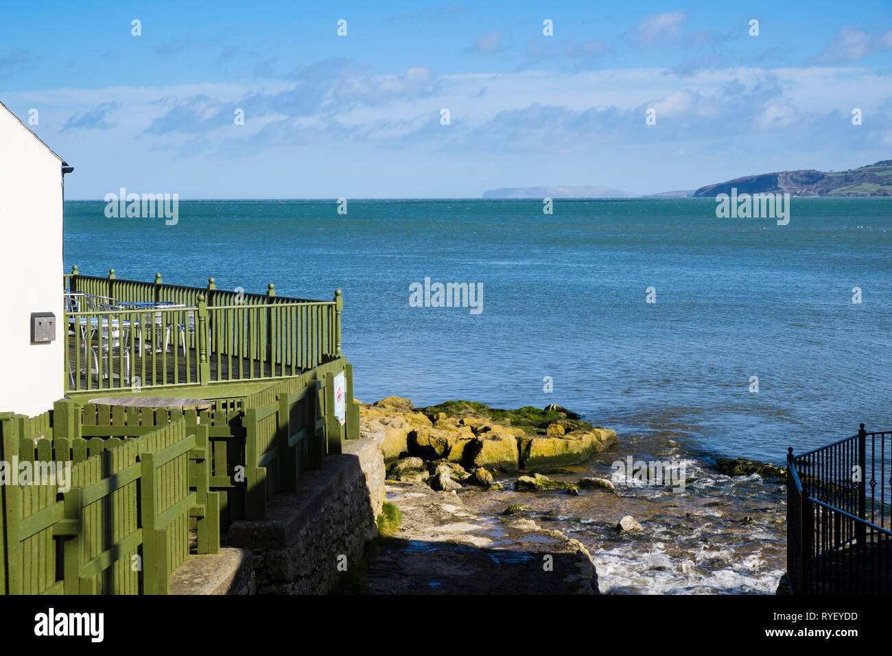 Bay Cafe e streaming sul litorale roccioso affacciato sul mare con Great Orme in distanza. Benllech, Isola di Anglesey, Galles del Nord, Regno Unito, Gran Bretagna Foto Stock