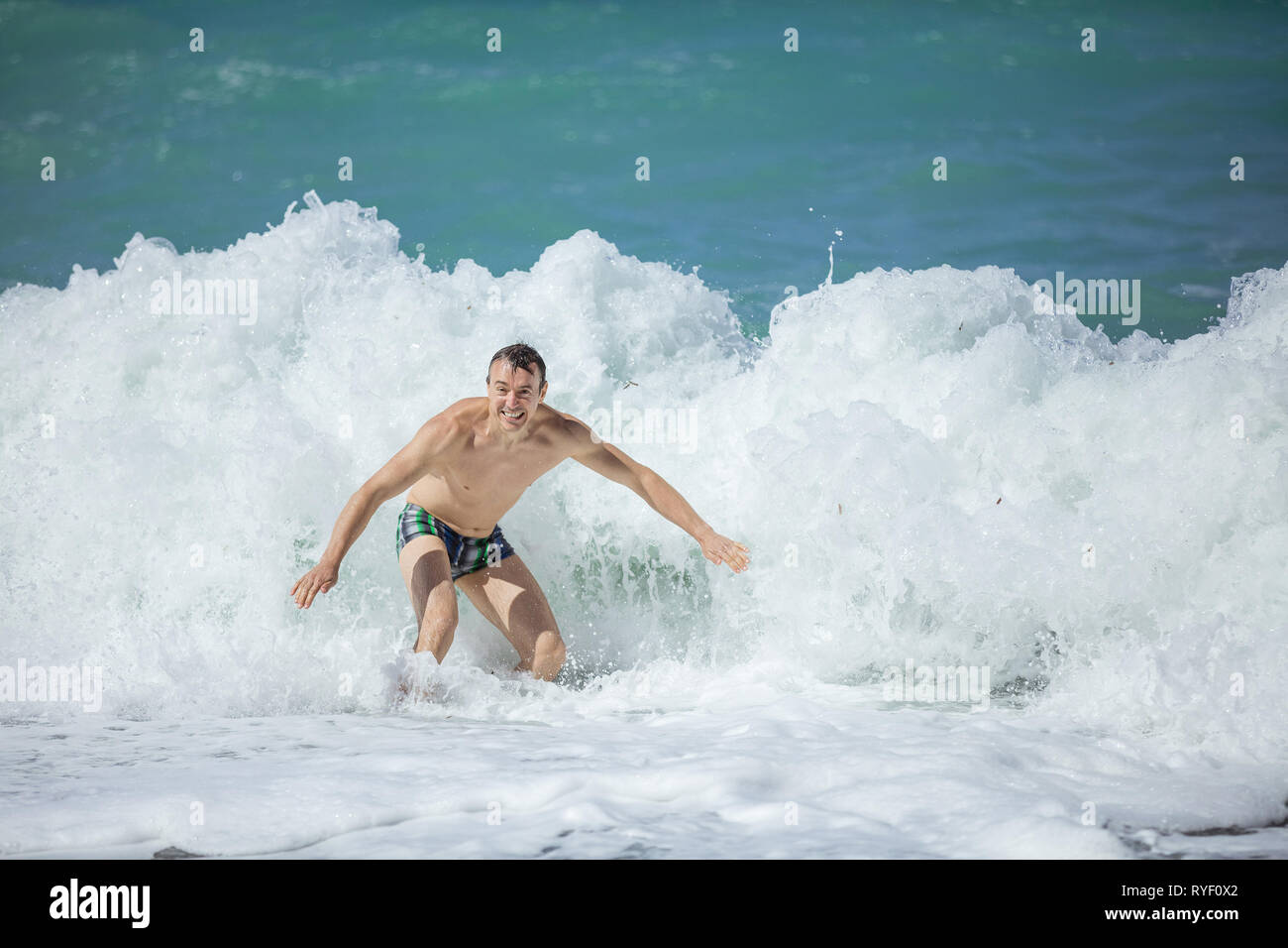 Giovane uomo godendo di onde alte in mare mosso, guardando la fotocamera e sorridente Foto Stock
