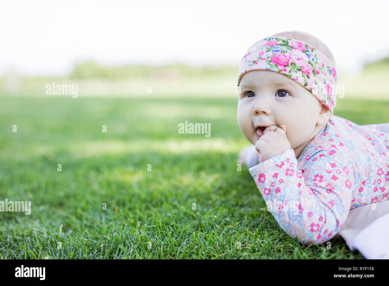 Carino bambina sdraiati sull'erba in estate park e guardando in alto Foto Stock