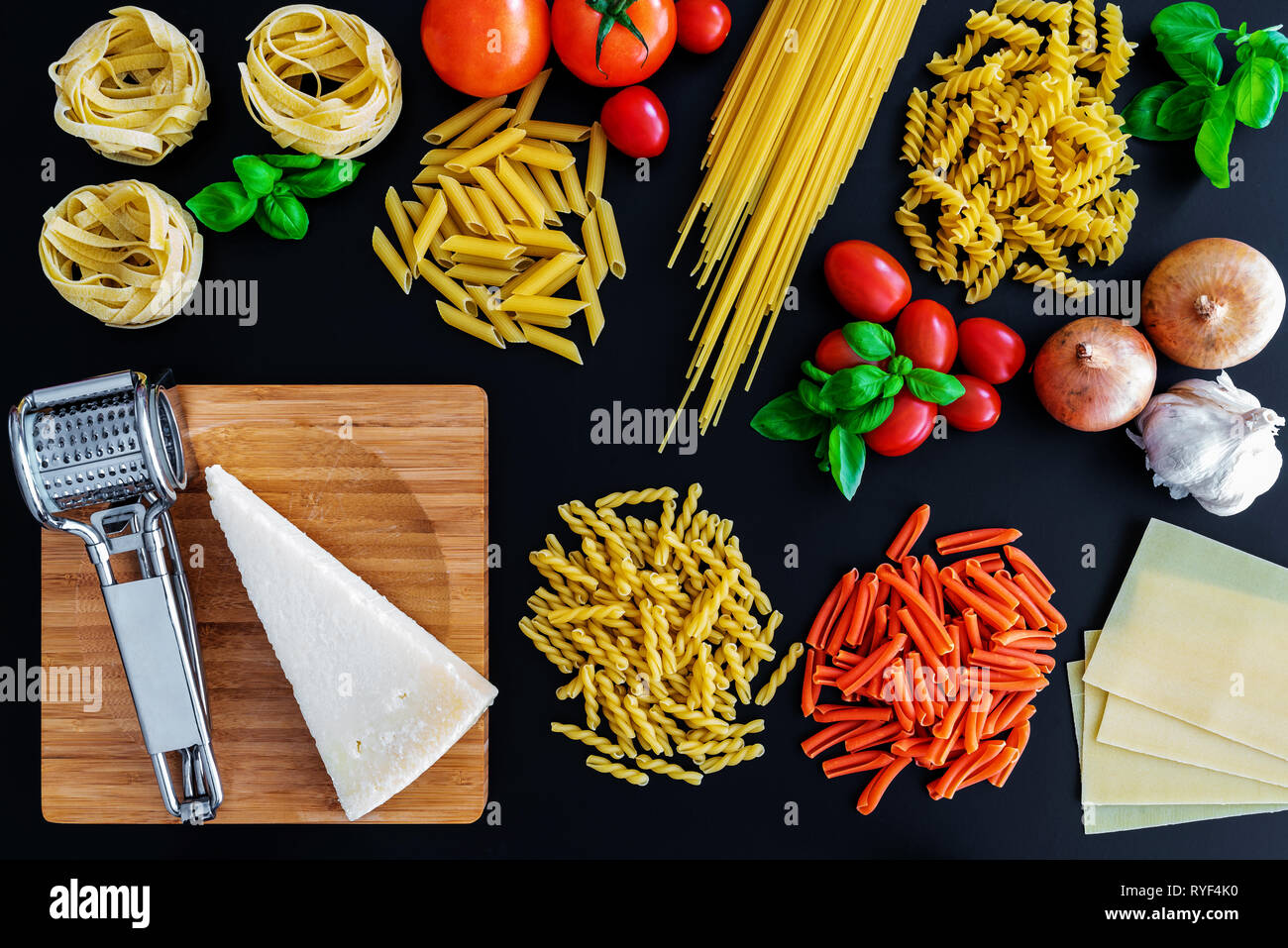 Non cotte diversi piatti di pasta italiana tagliatelle su sfondo scuro con foglie di basilico fresco, pomodori e cipolle Foto Stock